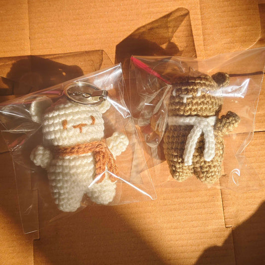 Two small crochet toys in clear plastic bags on a cardboard surface