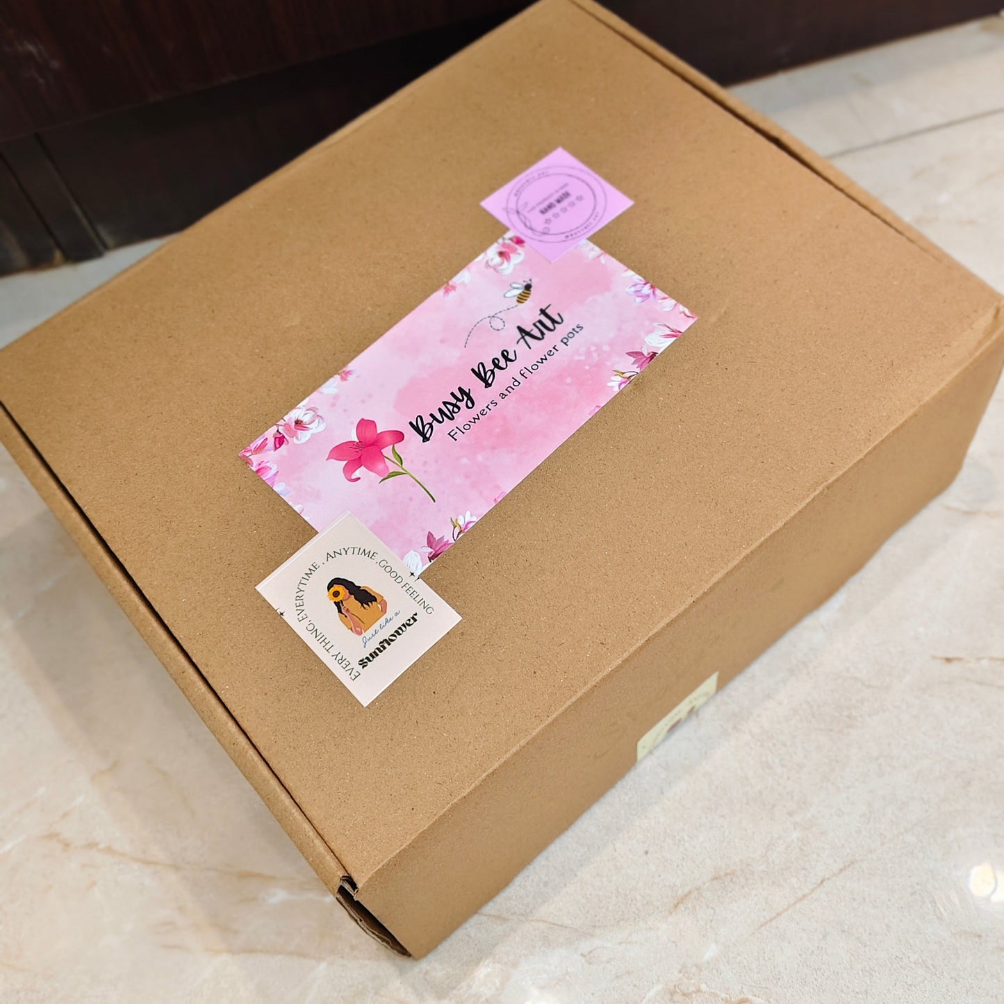 Cardboard box with a pink and white label on a tiled floor.