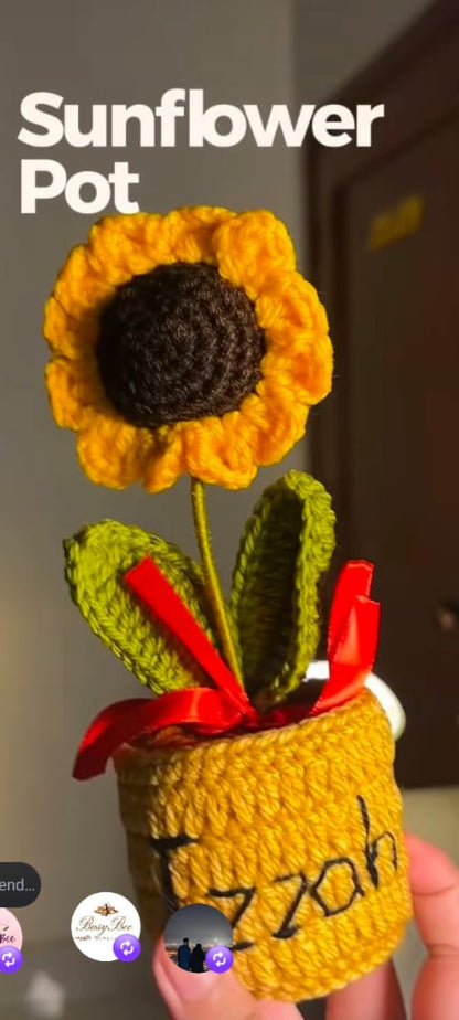 A crocheted sunflower pot holding a yellow and brown crocheted sunflower with green leaves and a red ribbon, held in a hand against an indoor background. Large text reads 'Sunflower Pot'.