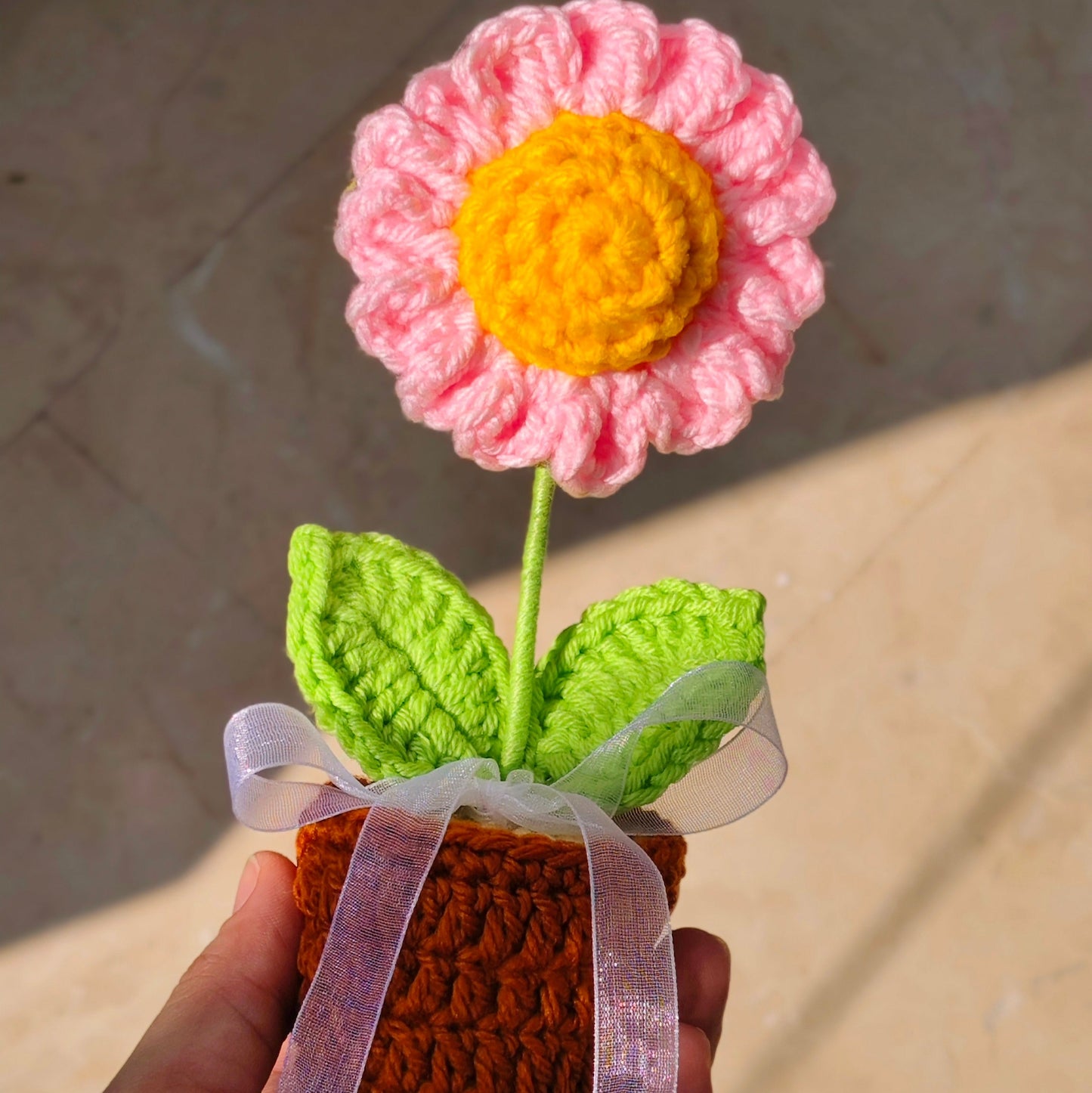 Handmade crochet flower in a pot held by a hand on a neutral background
