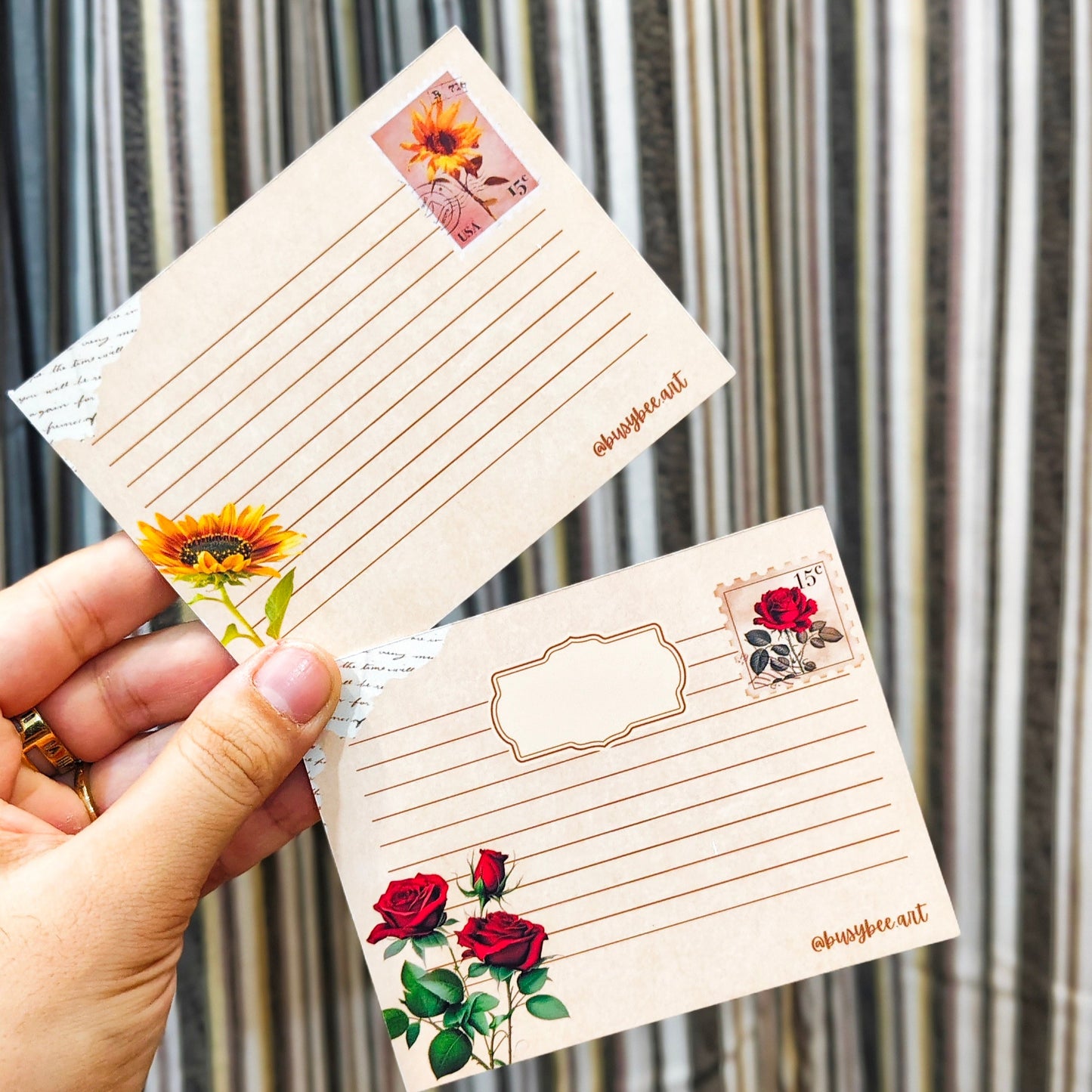 Hand holding two decorative postcards with floral designs against a striped background
