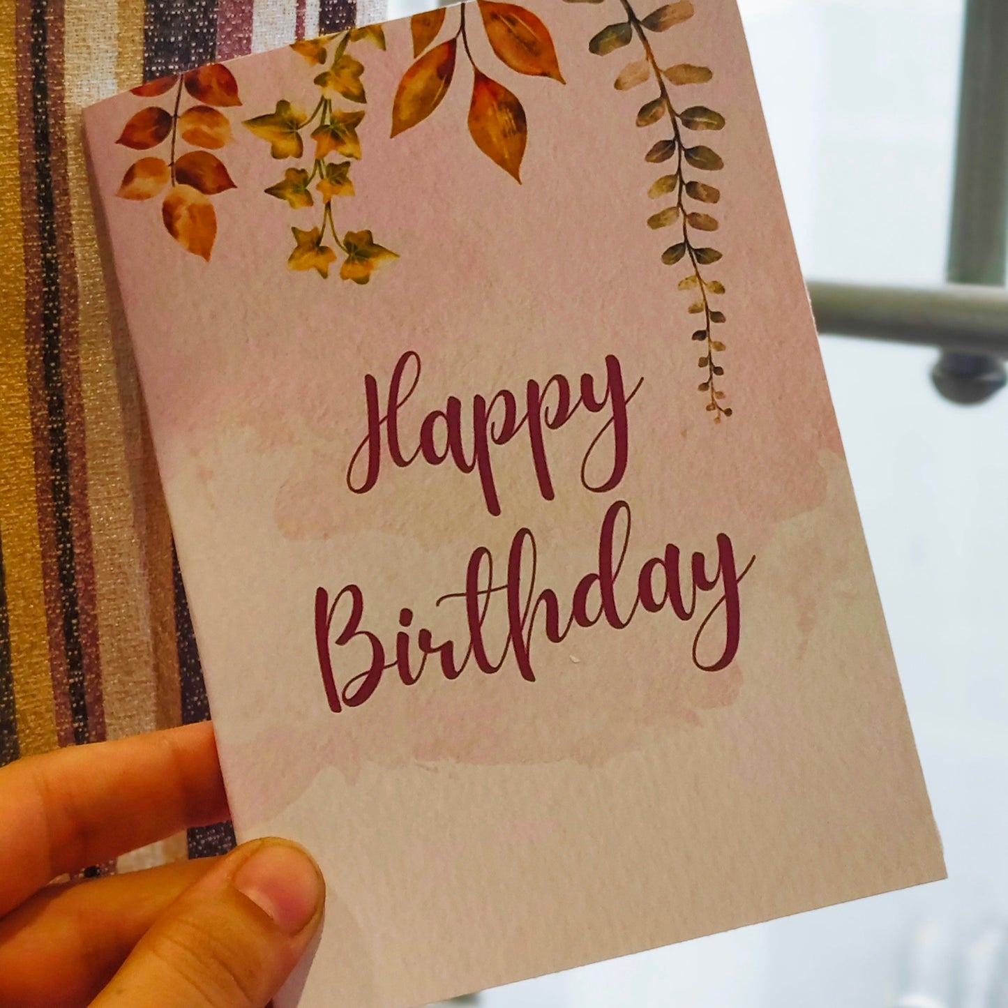 Hand holding a birthday card with floral designs and 'Happy Birthday' text.