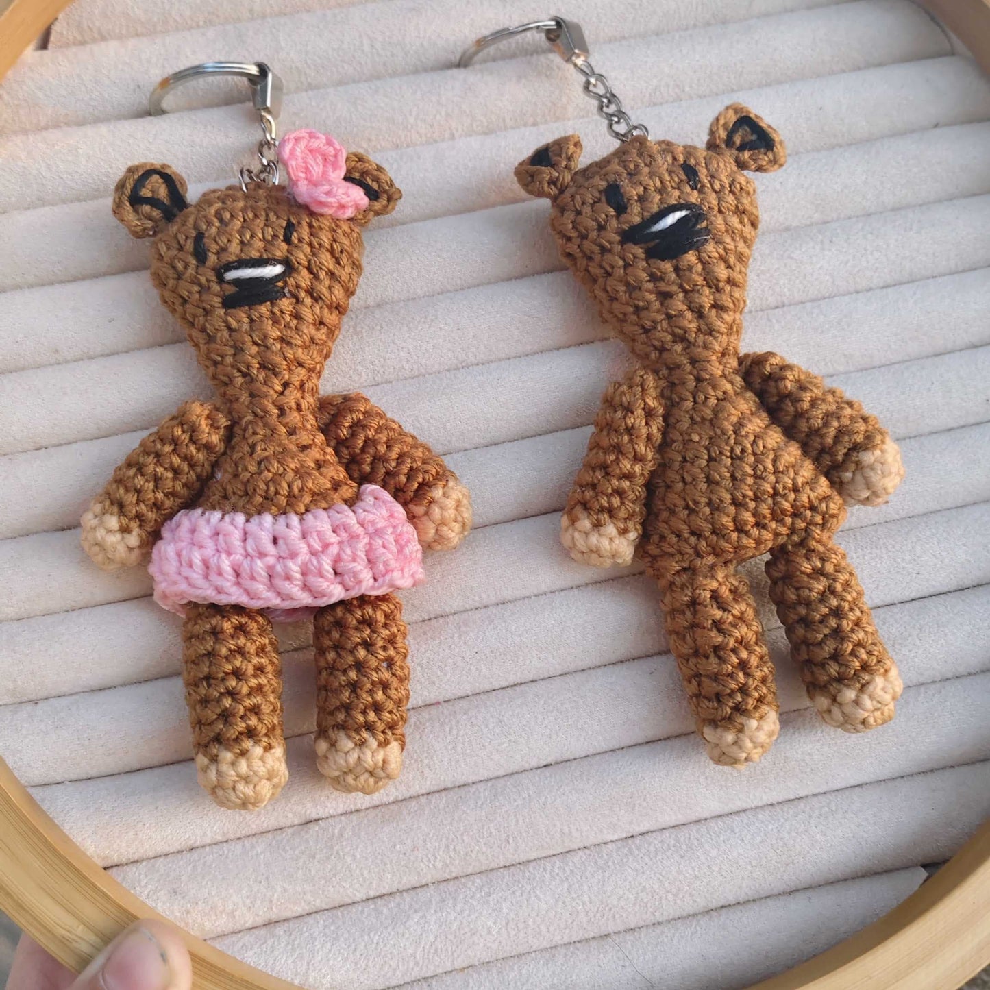 Two crochet teddy bear keychains on a wooden hoop with a blurred background.