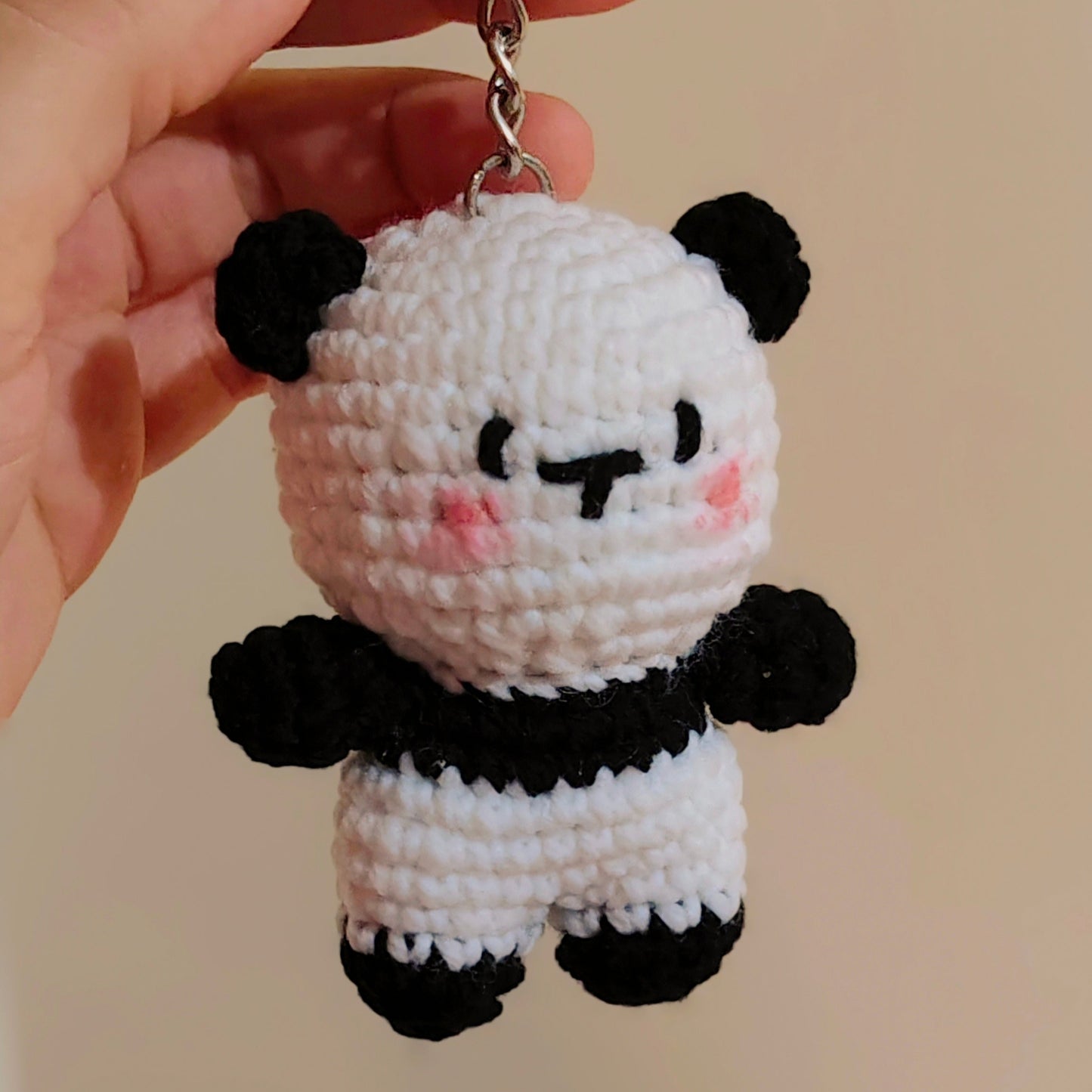 Crocheted panda keychain held by a hand against a beige background