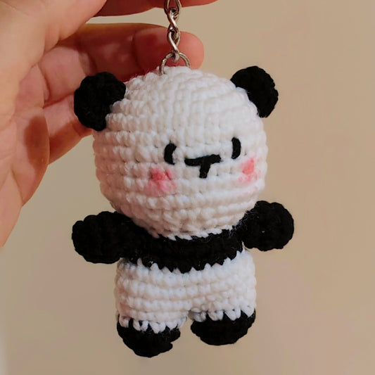 Crocheted panda keychain held by a hand against a beige background