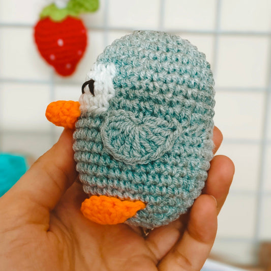 Hand holding a small crocheted penguin toy with a blurred background