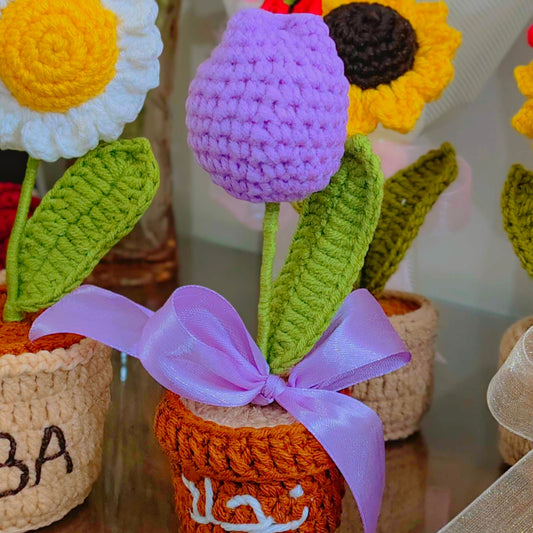 Crocheted purple tulip pots with flowers and ribbons on a reflective surface