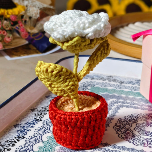 Knitted white rose in a pot on a patterned surface