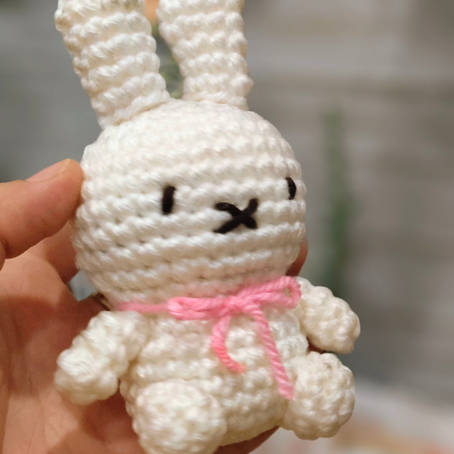 Hand holding a white crochet bunny with a pink bow against a blurred background