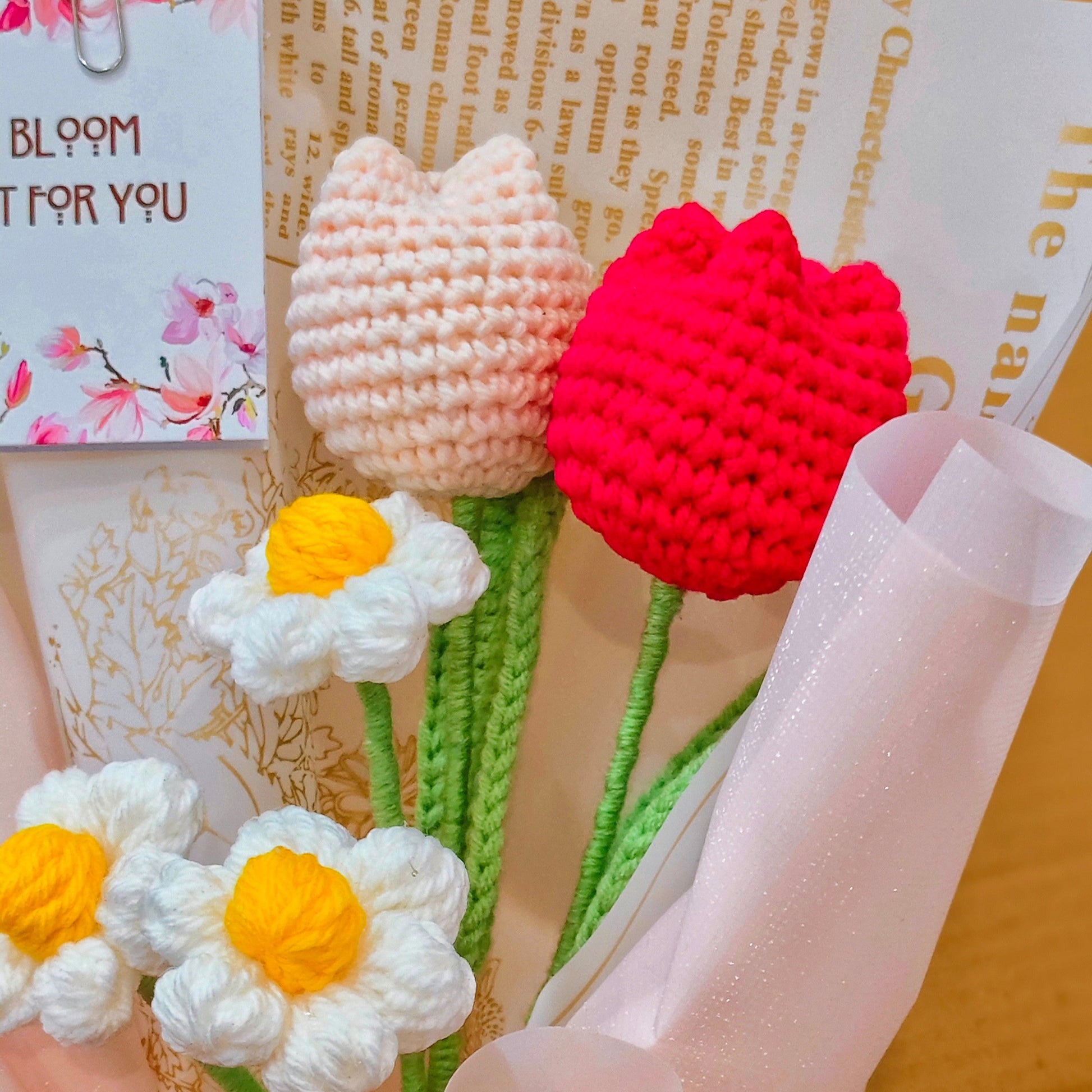 Knitted flowers in red, white, and yellow held by a hand with a blurred background
