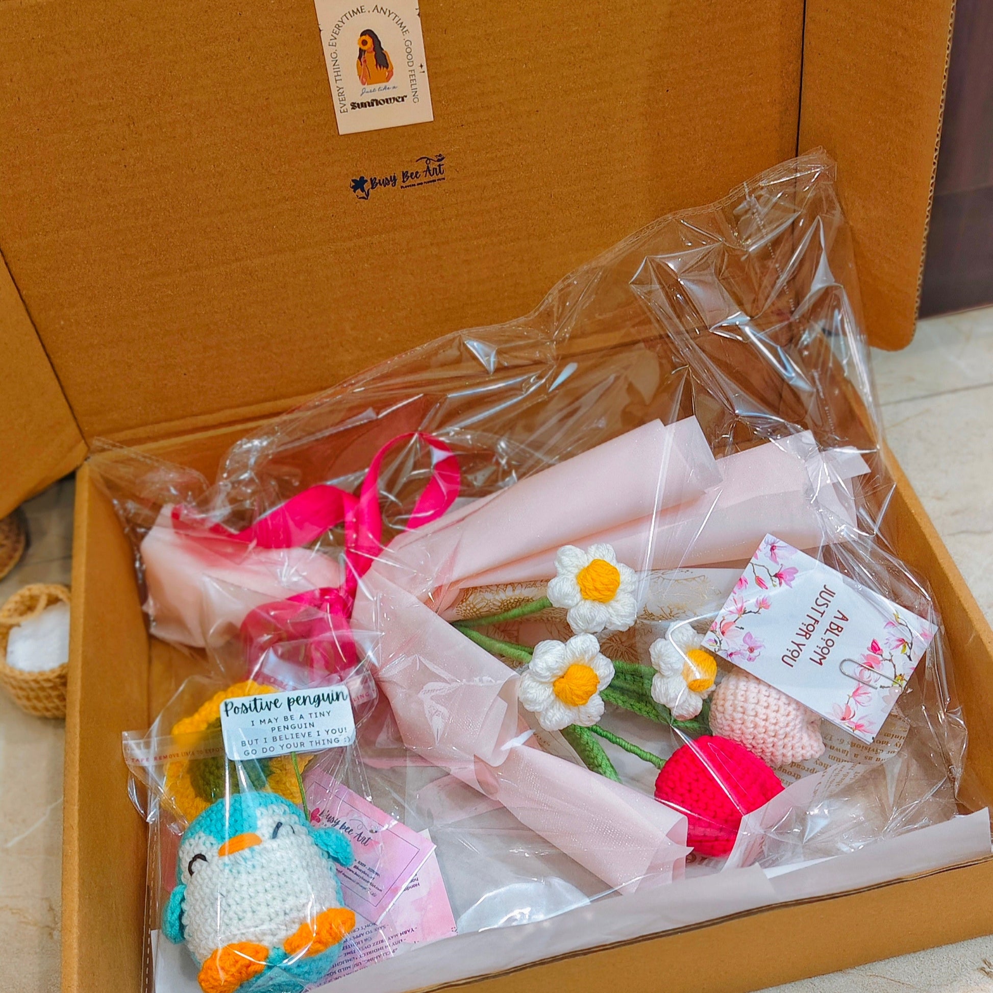 Gift set with plush toys and flowers in a cardboard box on a tiled floor.