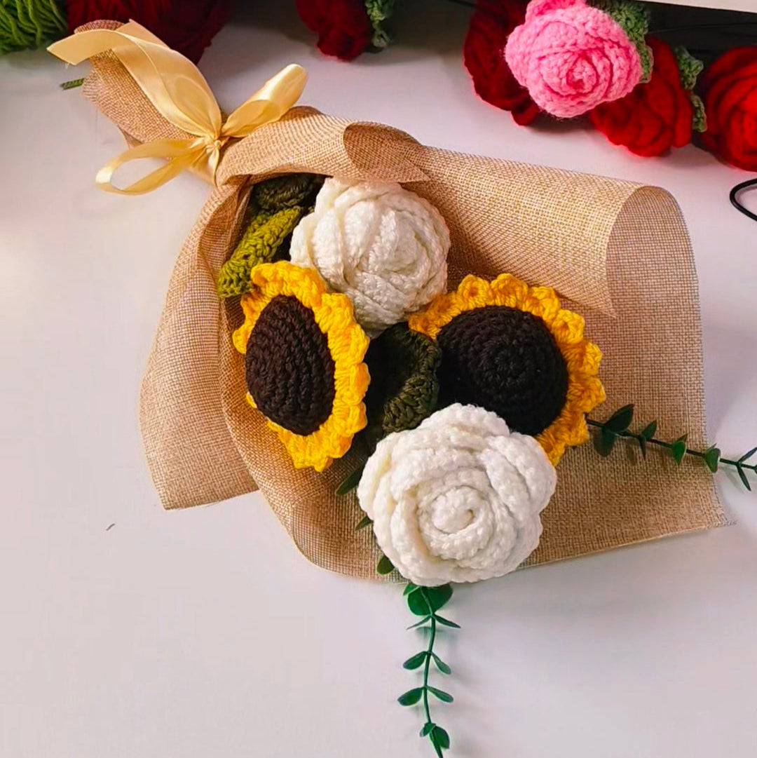 Crocheted sunflower and rose bouquet on a white surface with a blue organizer in the background.