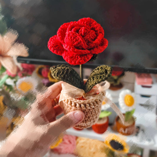 Hand holding a small crocheted red rose in a basket with a blurred background
