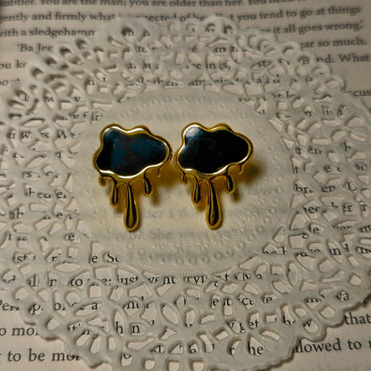 Black cloud-shaped earrings with gold accents on a textured paper background
