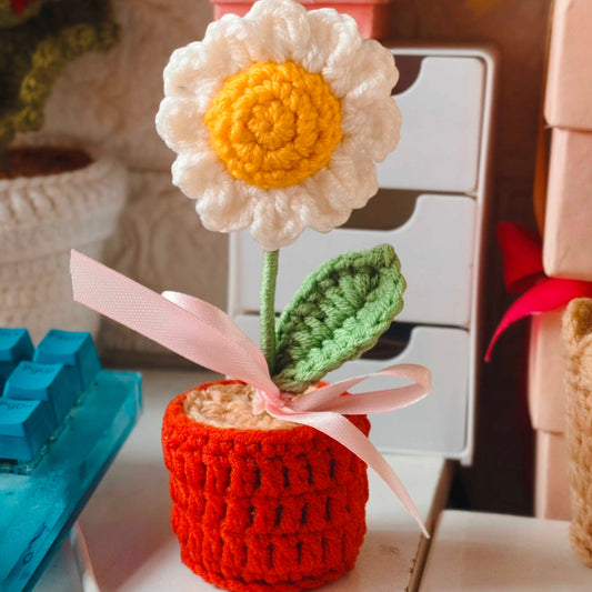 daisy flower in an orange pot with a pink ribbon on a white surface.