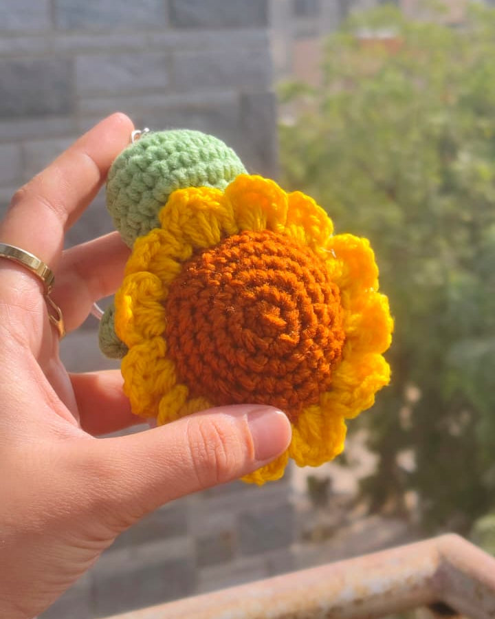 Hand holding a crocheted sunflower with a blurred outdoor background