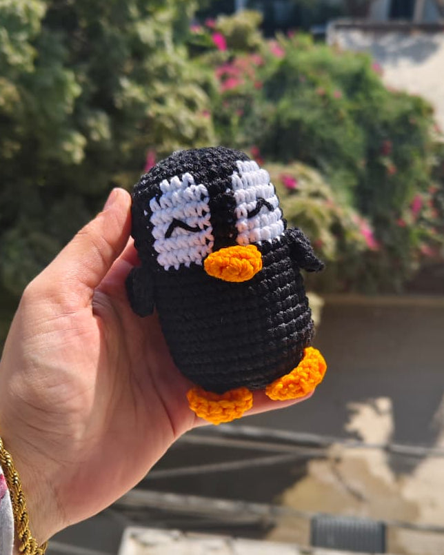 Hand holding a small crocheted penguin toy with a blurred outdoor background
