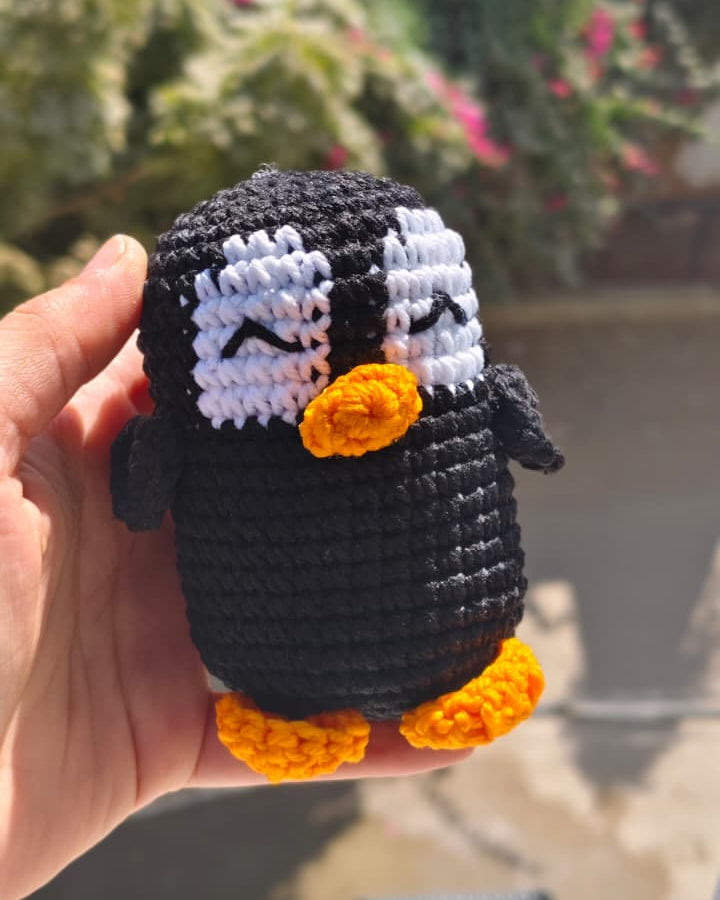 Hand holding a small crocheted penguin toy with a blurred outdoor background