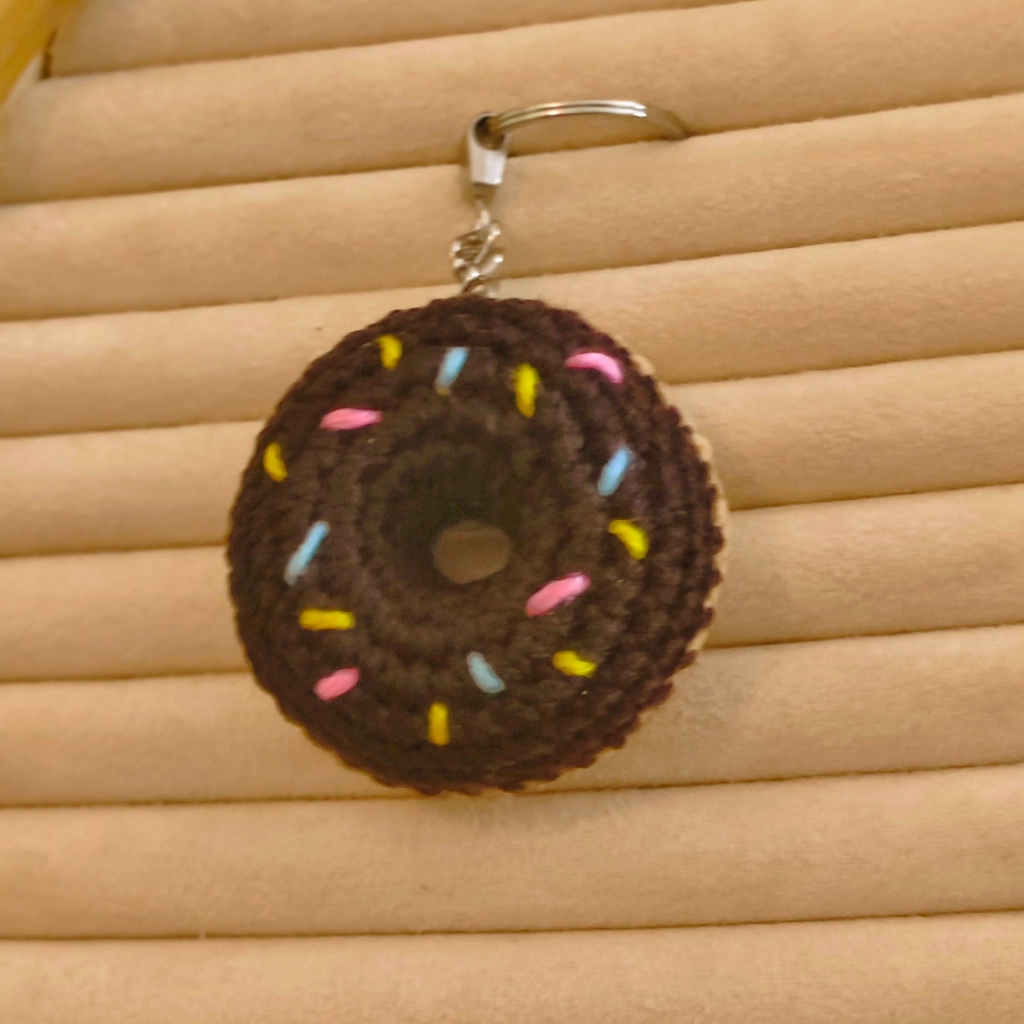 Crocheted donut keychain with colorful sprinkles on a beige woven surface