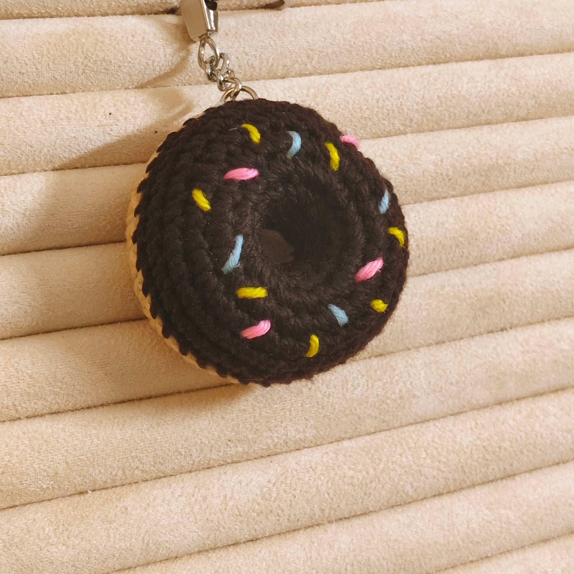 Donut-shaped keychain with colorful sprinkles on a beige textured surface