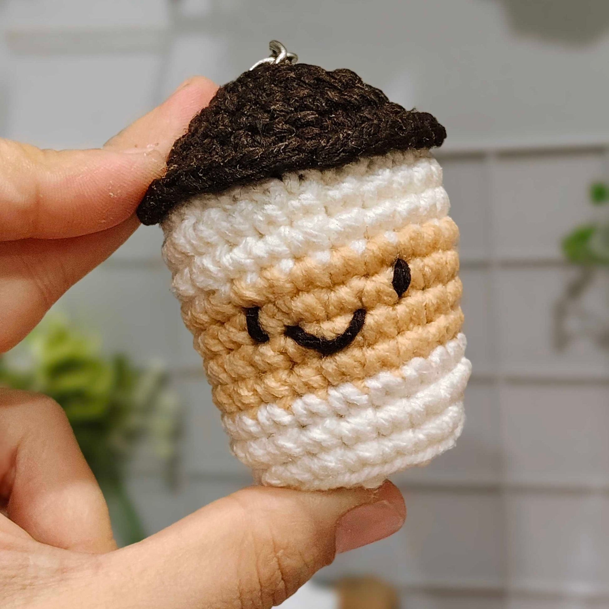 Hand holding a small crocheted character with a brown hat and white body.