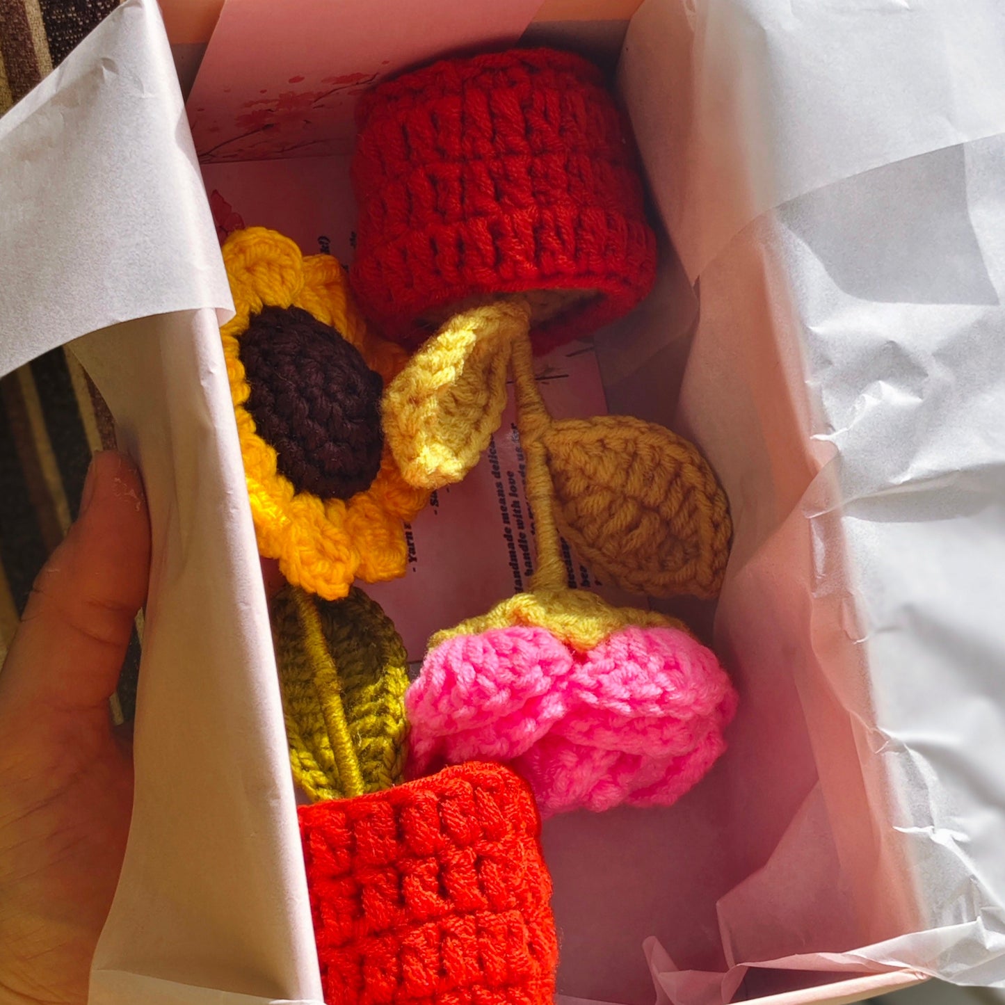 Colorful crocheted flowers in a box held by a hand.
