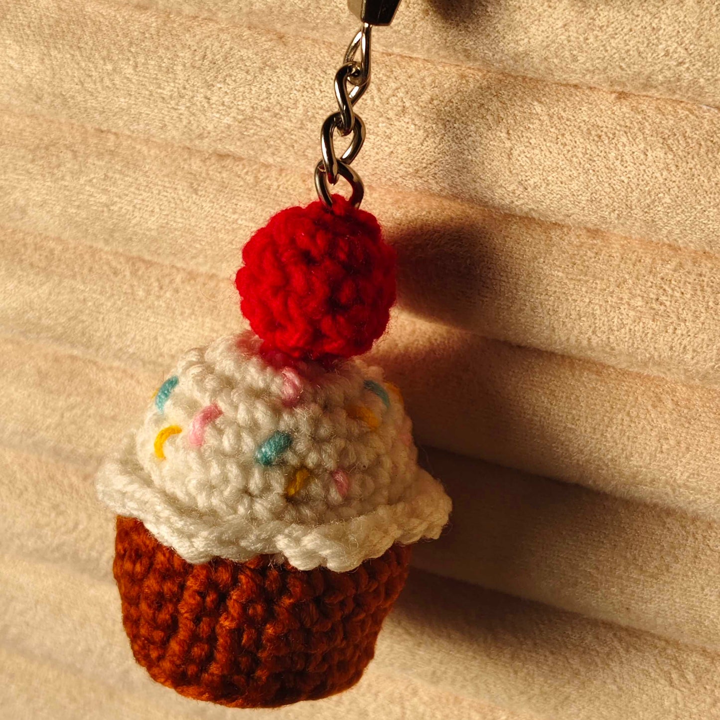 Crocheted cupcake keychain with a red cherry on top against a beige background