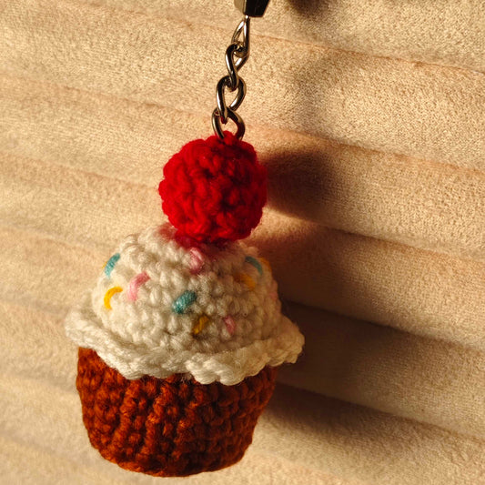 Crocheted cupcake keychain with a red cherry on top against a beige background