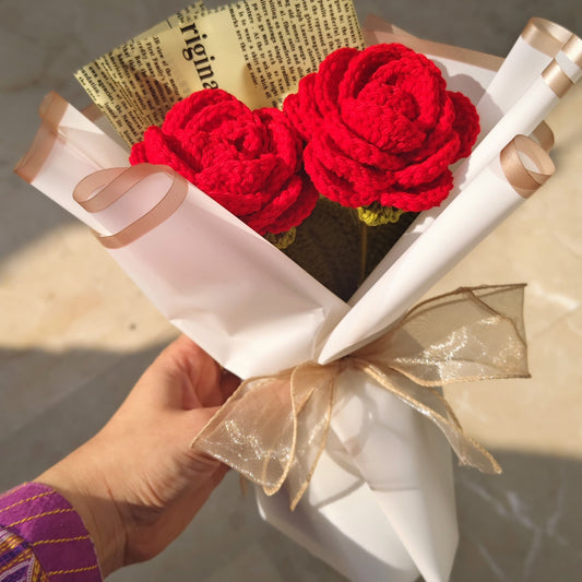 Bouquet of red flowers wrapped in white paper with a gold bow, held by a person.
