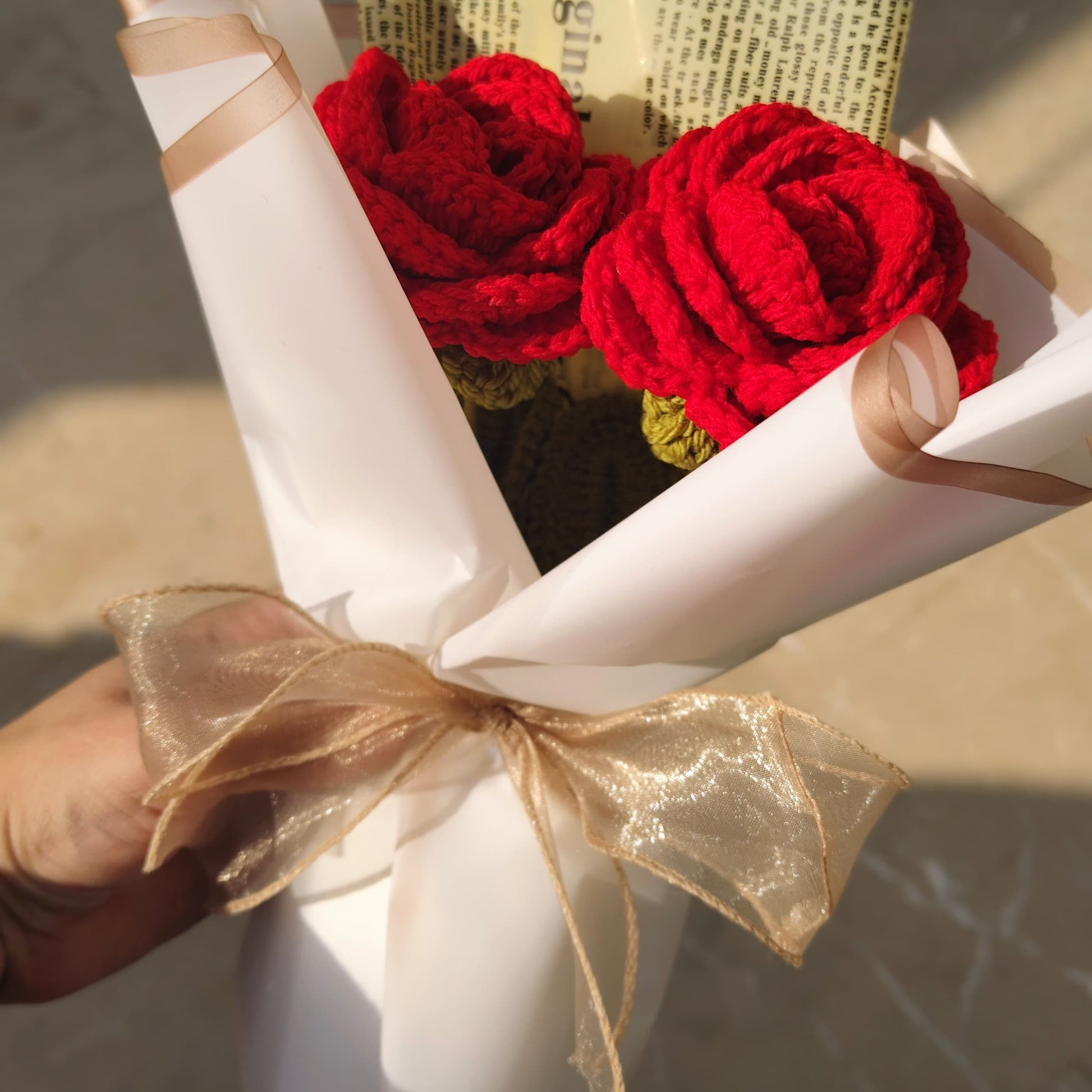 Bouquet of red roses wrapped in white paper with a gold ribbon, held by a hand.