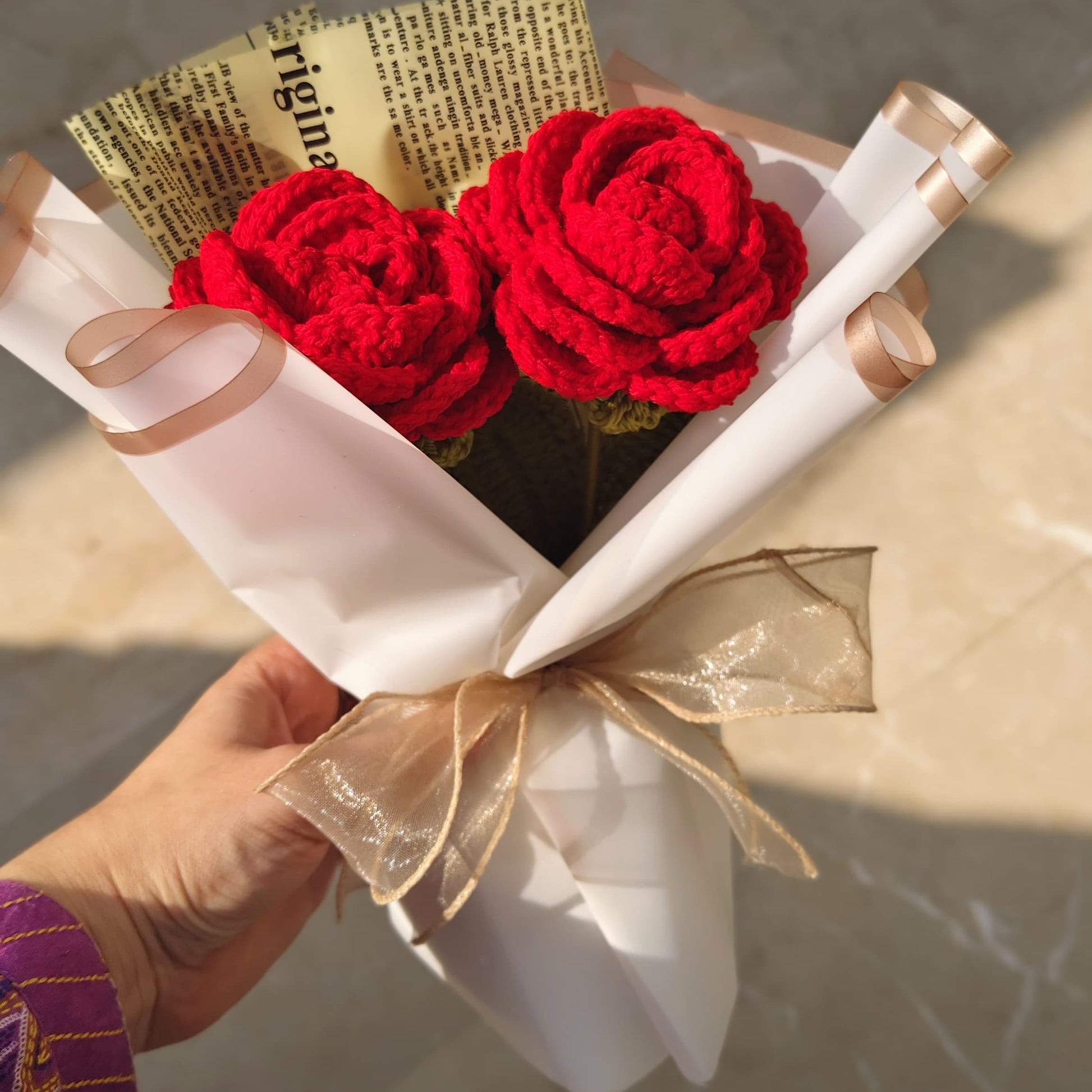 Bouquet of red flowers wrapped in white paper and gold ribbon held by a person.