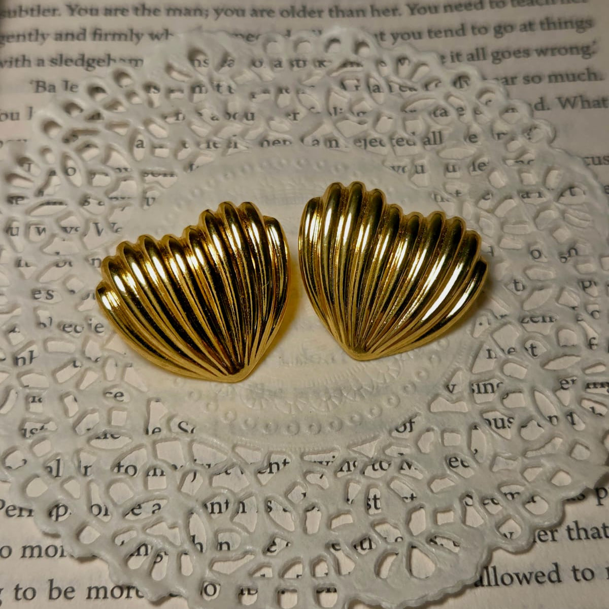 Gold shell-shaped earrings on a textured white surface with text.