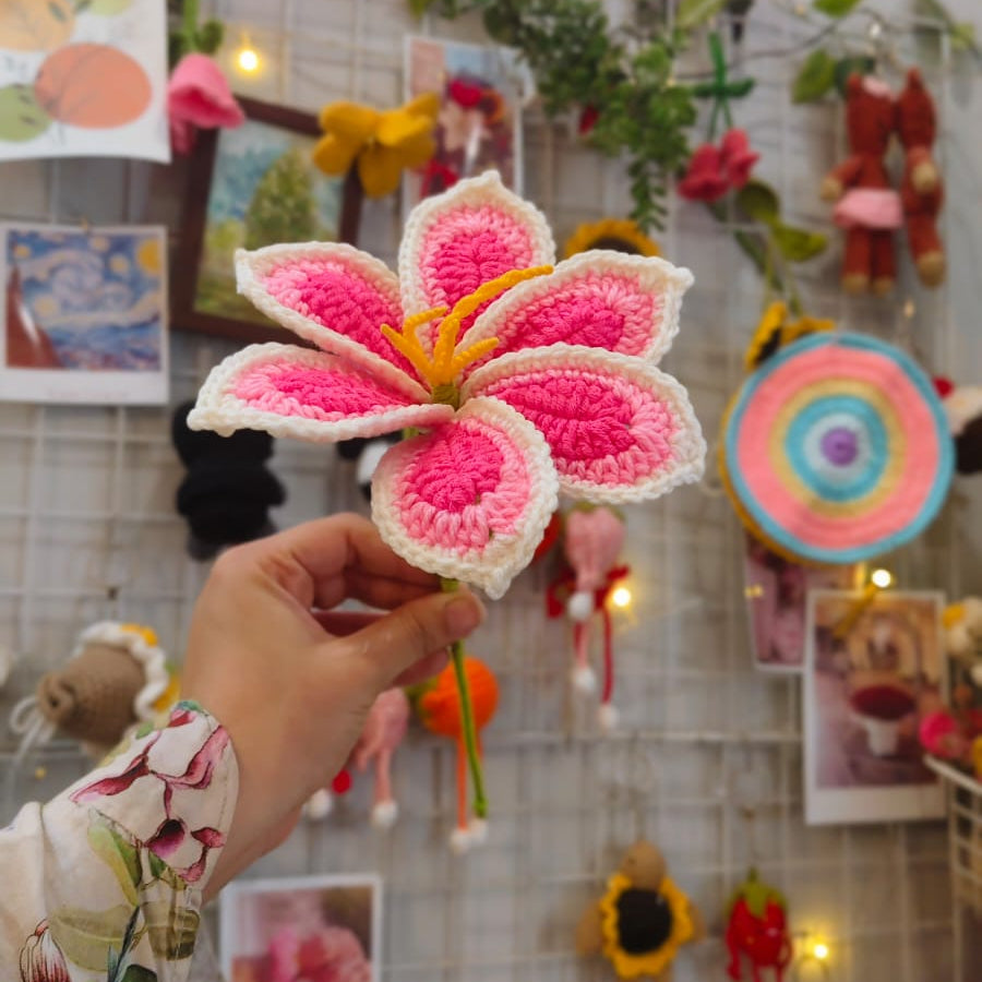 Hand holding a pink and white crocheted flower in front of a colorful wall with 'Bee Art' neon sign.
