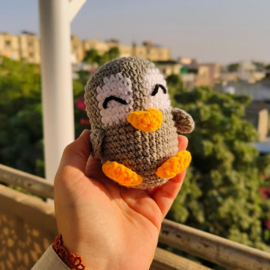Hand holding a small crocheted penguin toy with a cityscape in the background