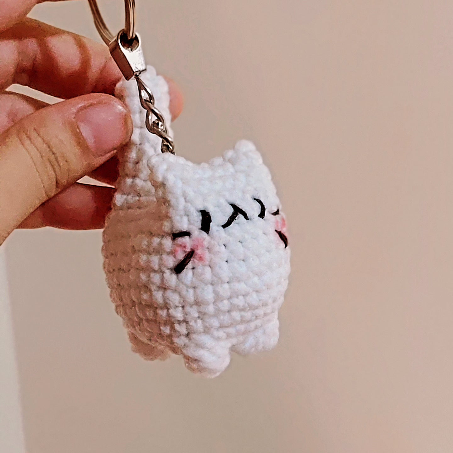 Hand holding a small crochet cat keychain against a plain background
