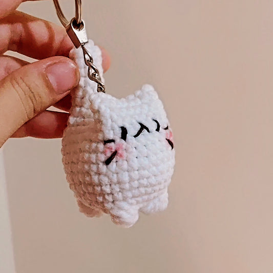 Hand holding a small crochet cat keychain against a plain background