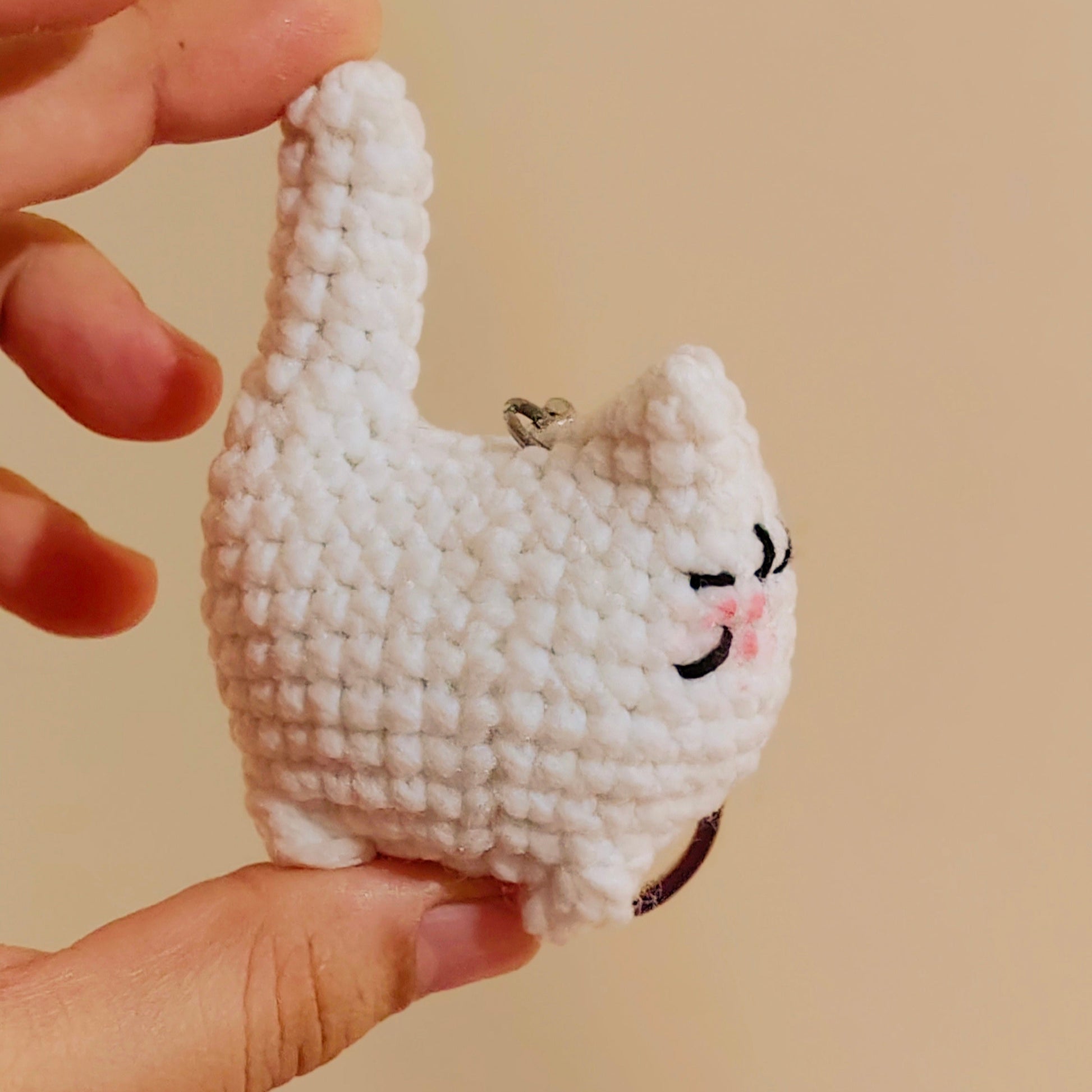 Hand holding a white crochet cat toy against a beige background