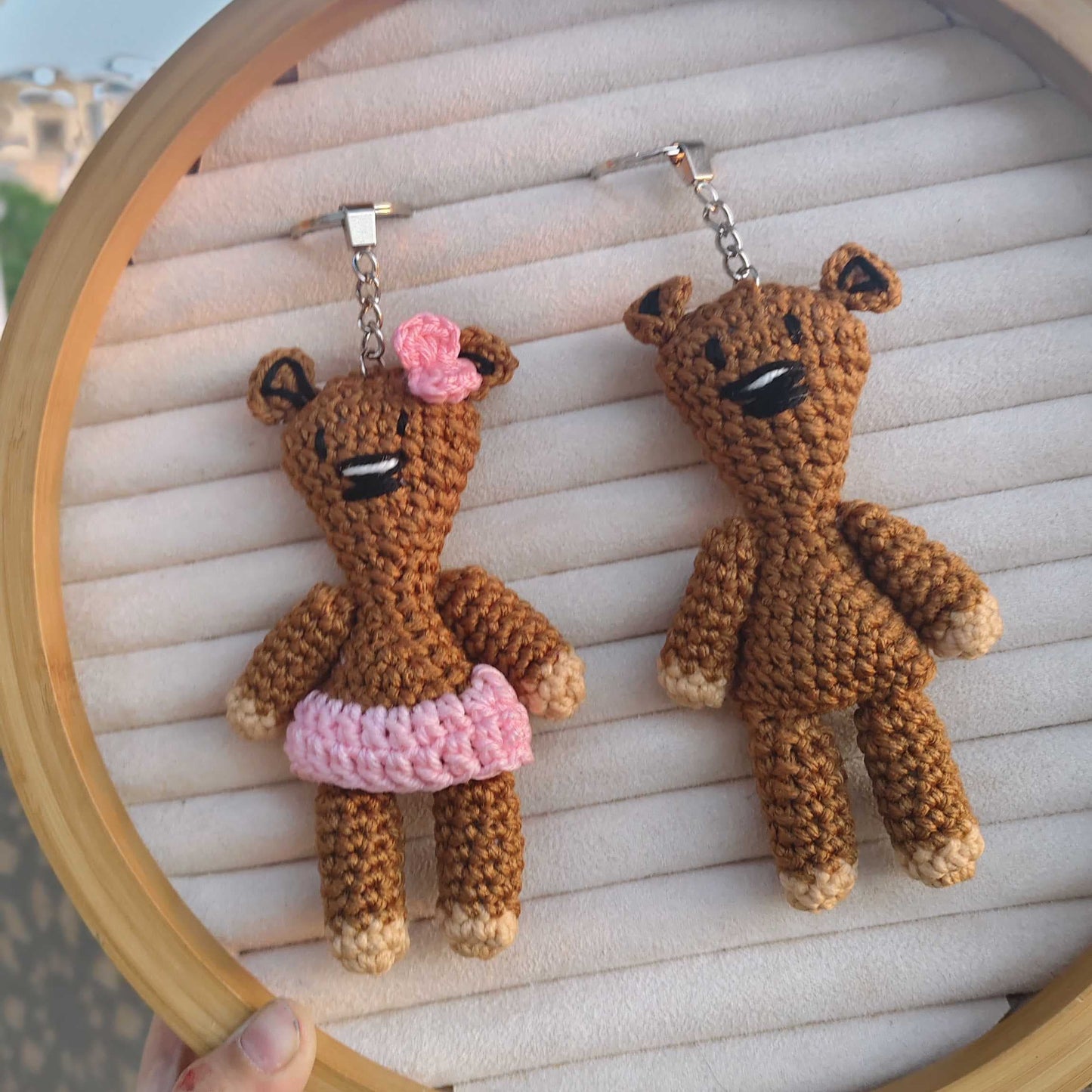 Two small brown teddy bear keychains on a wooden hoop with a blurred background.