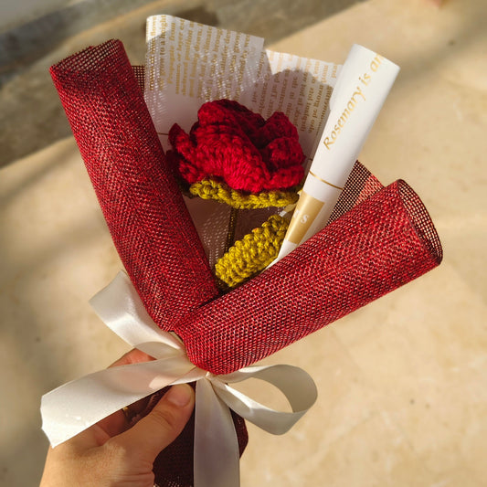 Bouquet of red, yellow, and white flowers wrapped in red mesh with a white ribbon, held by a hand.