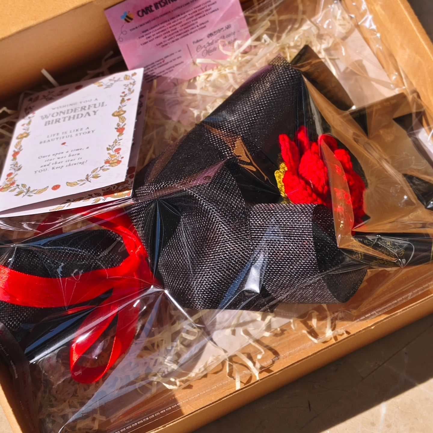 Open box containing various items including a red ribbon, black fabric, and a card with text.