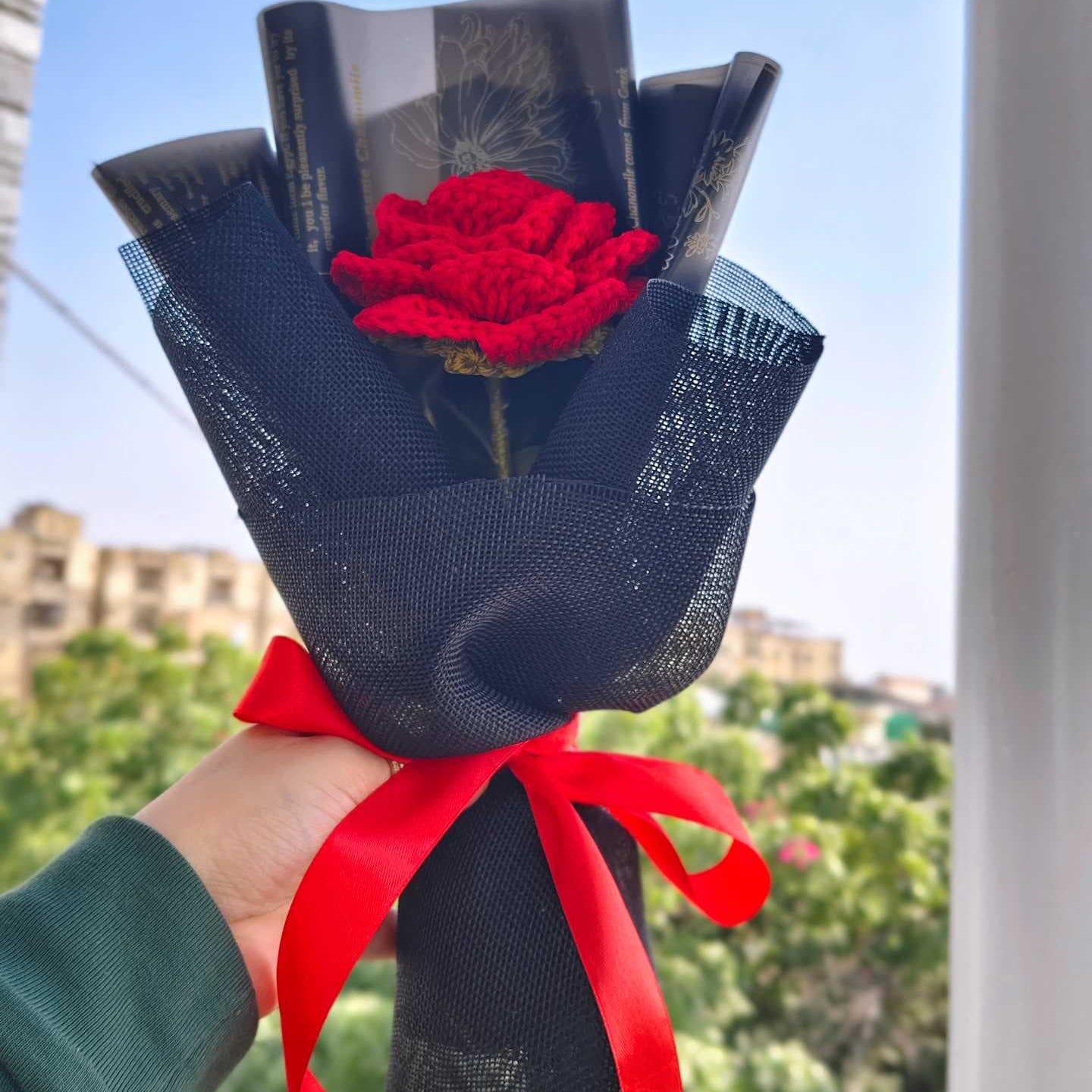 Bouquet of red roses wrapped in black paper with a red ribbon held against a blue sky.