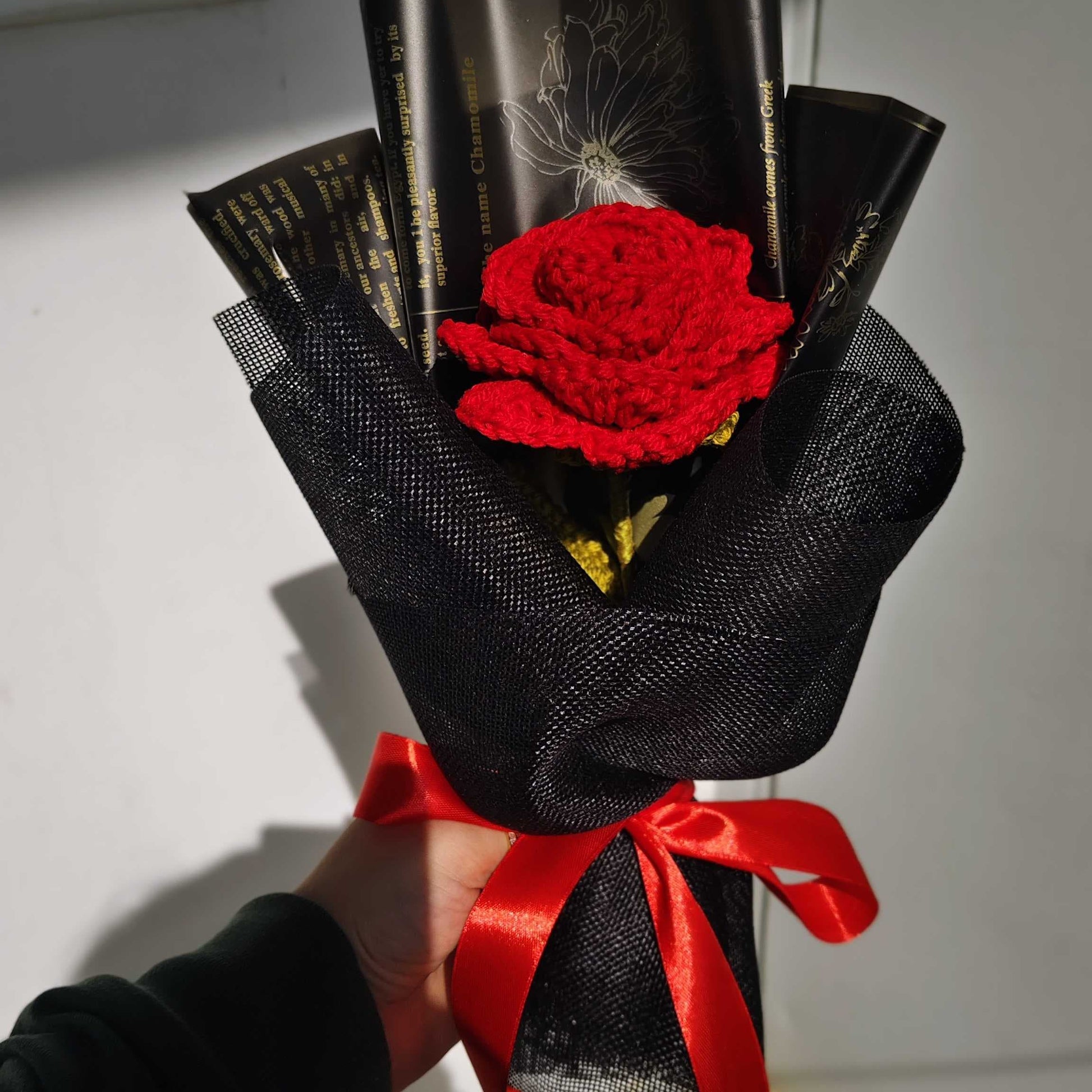 Bouquet with a red rose wrapped in black paper and tied with a red ribbon, held by a person.