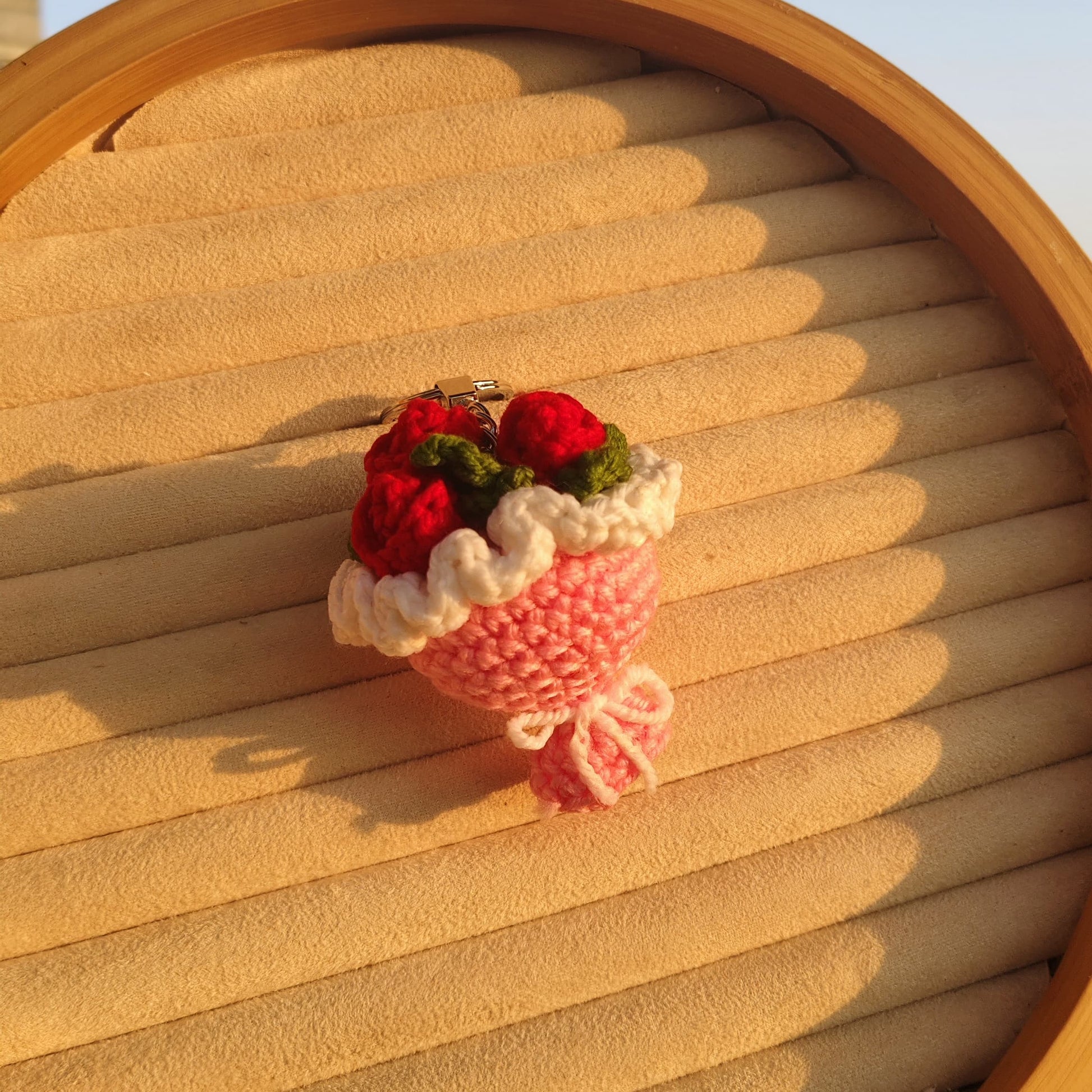 Small knitted strawberry bouquet on a wooden surface with a blurred outdoor background