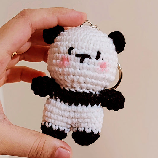 Hand holding a small crocheted panda keychain against a beige background