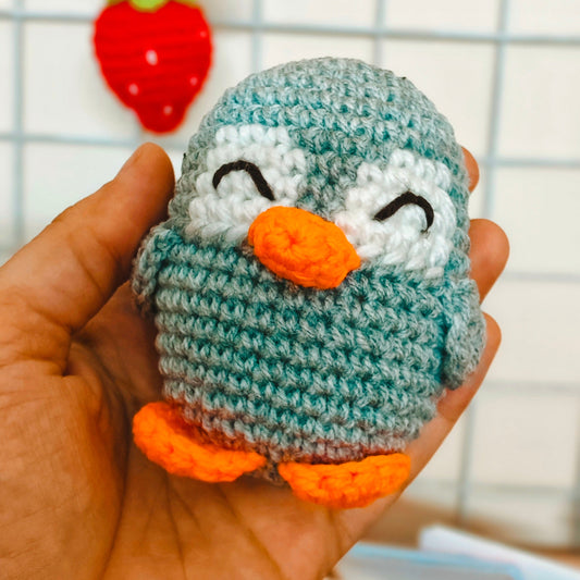Hand holding a small crocheted penguin toy with a blurred background