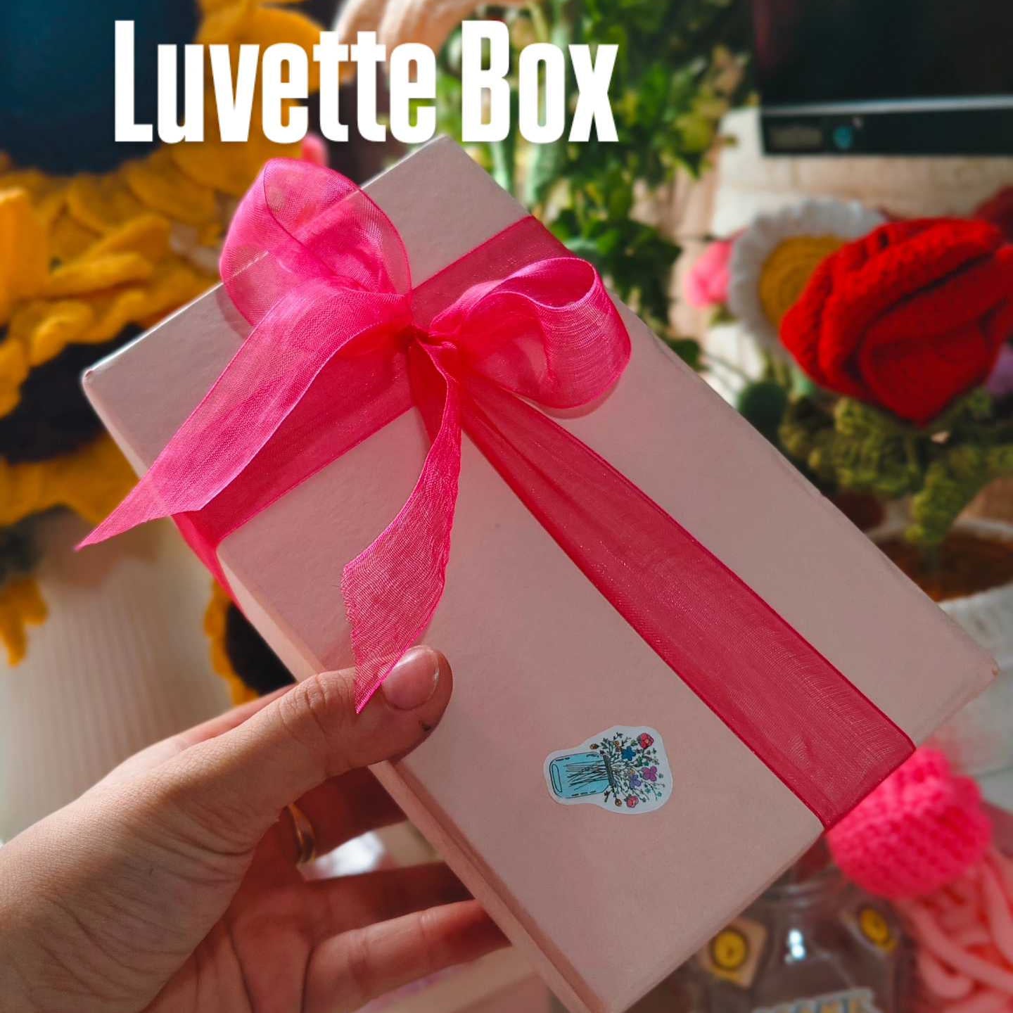 Pink gift box with a pink ribbon held by a hand, with 'Luvette Box' text above.