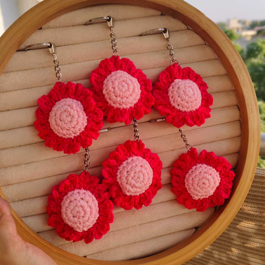 Red and pink crochet flower earrings on a wooden stand outdoors.