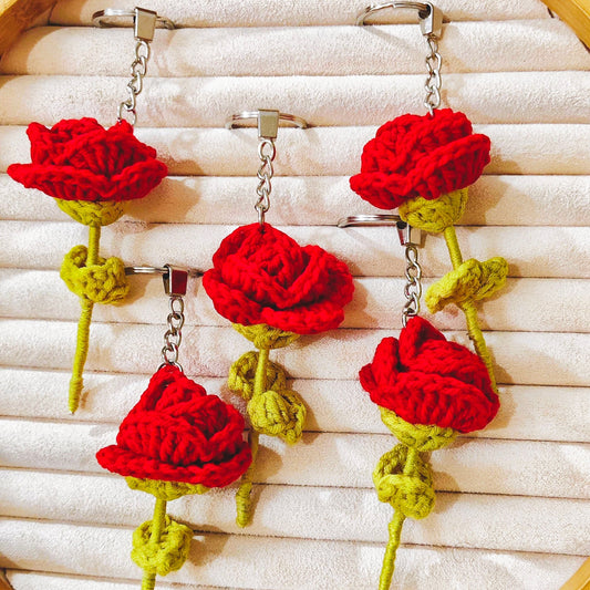 Red and green crocheted rose keychains  on a wooden hoop with white fabric background