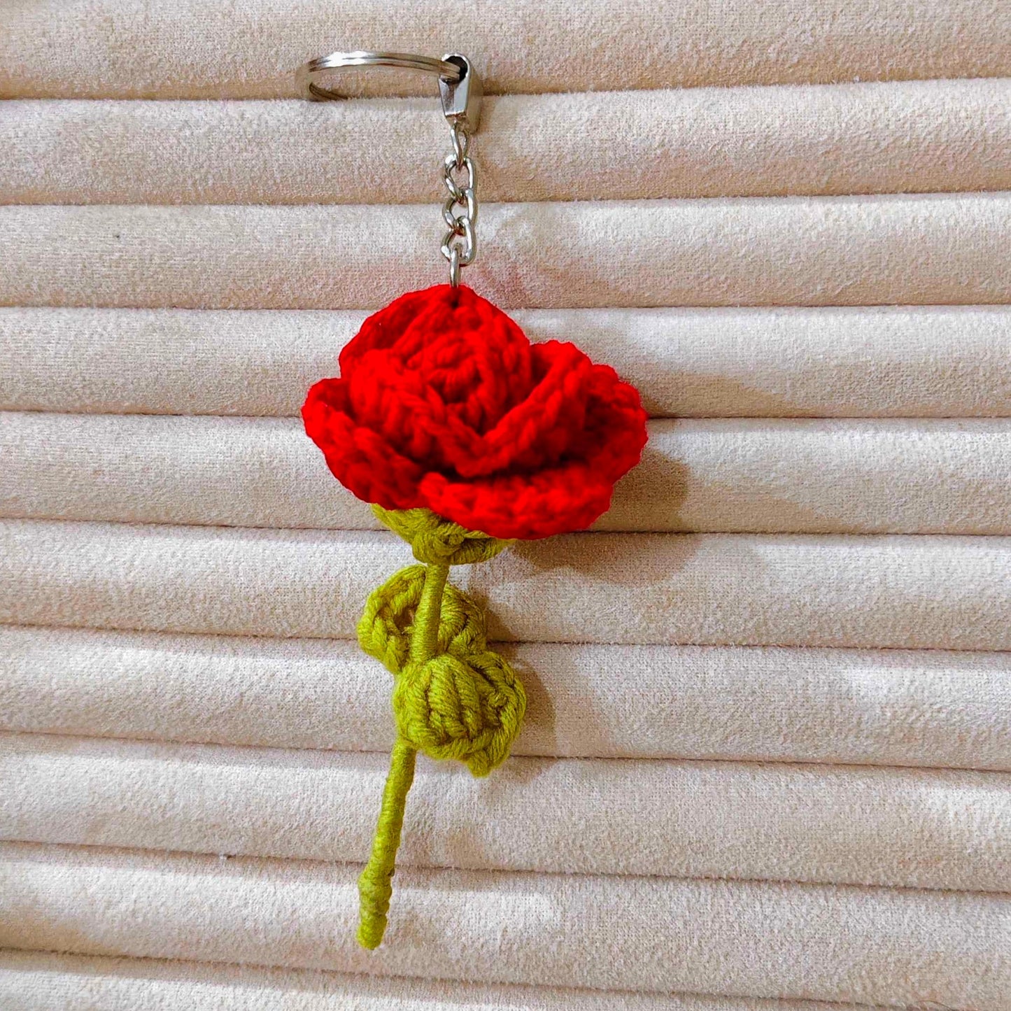 Red crocheted rose keychain on a textured beige background