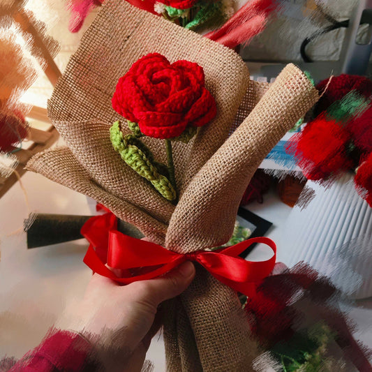 Bouquet with red rose and burlap wrap held by a hand, with blurred background